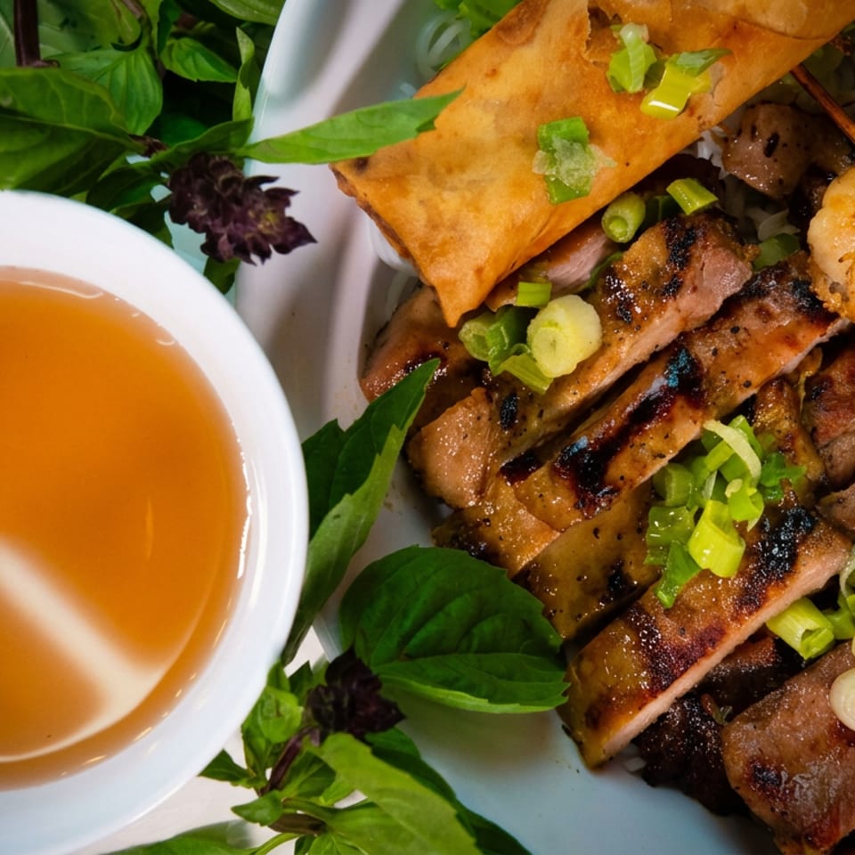 Grilled shrimp, sliced pork, and an egg roll with a side of dipping sauce and basil.